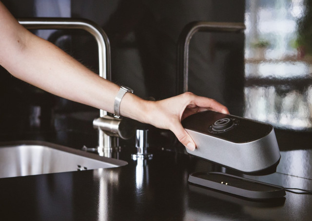 Un bras qui pose une enceinte nomade sur la planche de travail dans la cuisine