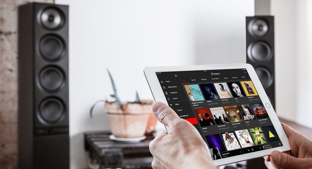 tablette avec application de streaming musicale en premier plan et enceintes en arrière plan