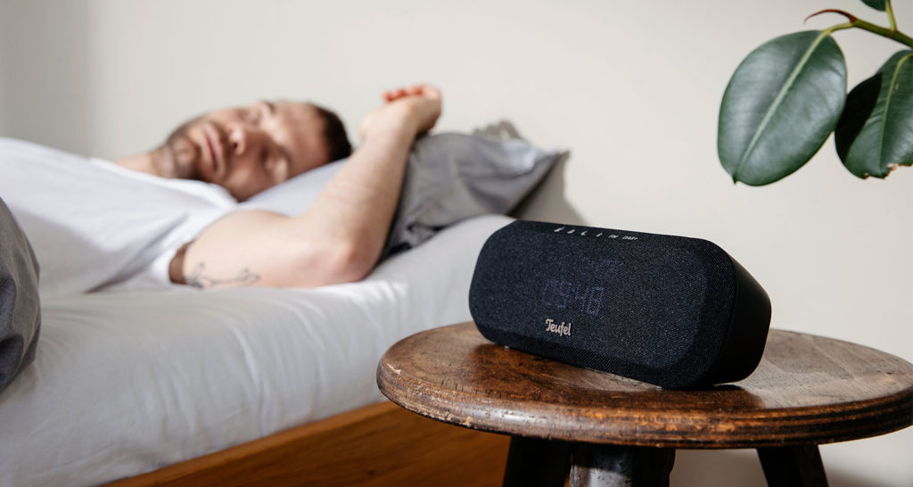 Homme se réveillant dans son lit à côté d'une radio et d'une plante, propice à une thérapie sonore