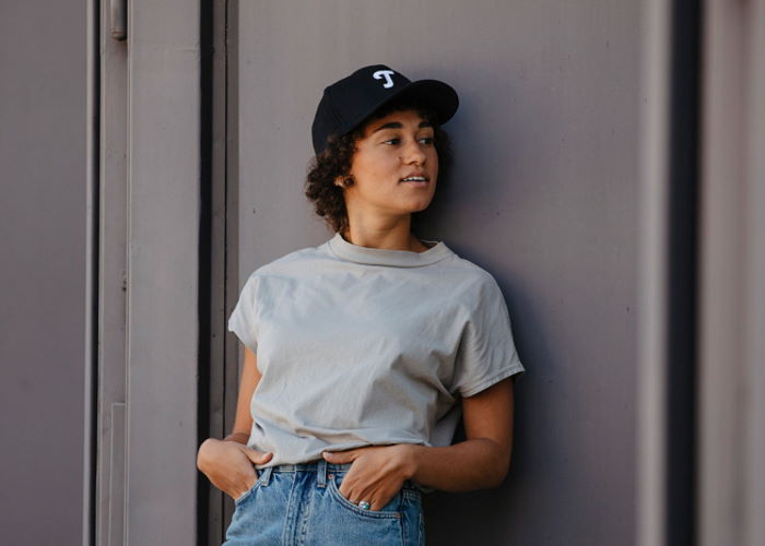 Jeune femme avec une casquette Teufel « T » appuyée contre un mur