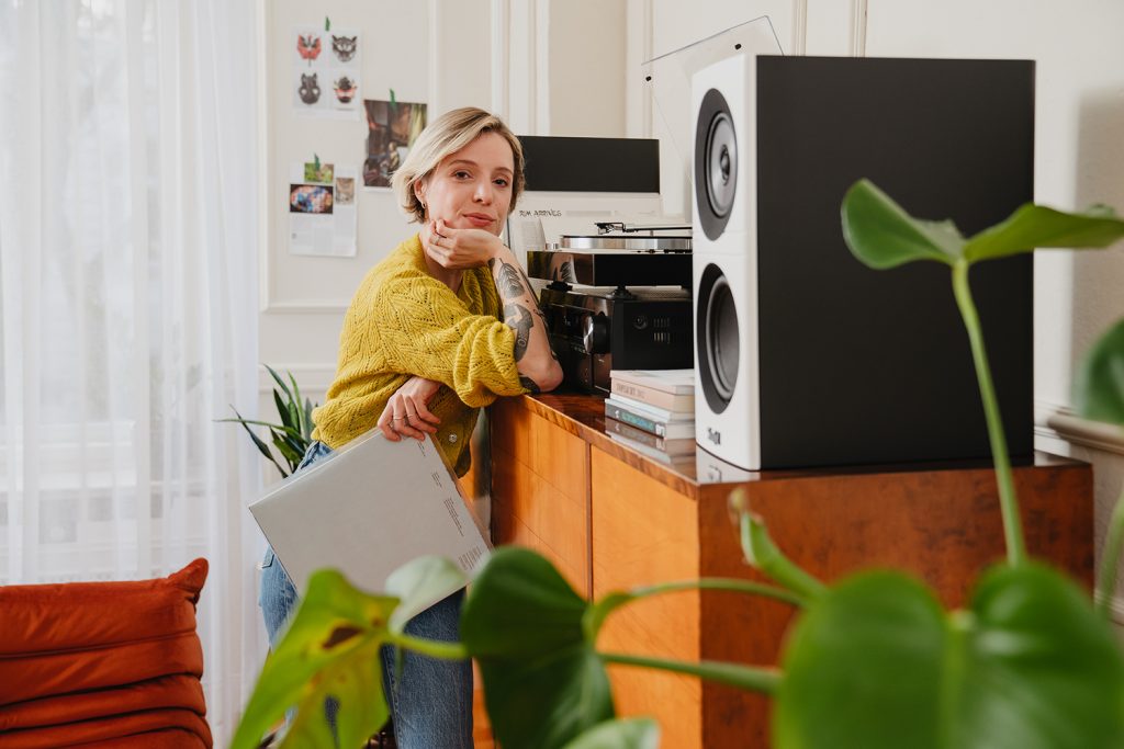 femme pose un bras sur son meuble devant sa plateforme vinyle., sopn système d'enceintes Teufel et ses vinyles, dans son salon