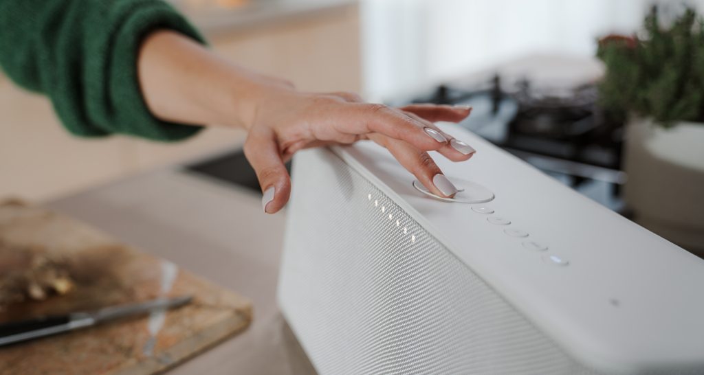 Une femme dans sa cuisine, en train de cuisiner, augmente le volume de son enceinte MOTIV HOME Teufel