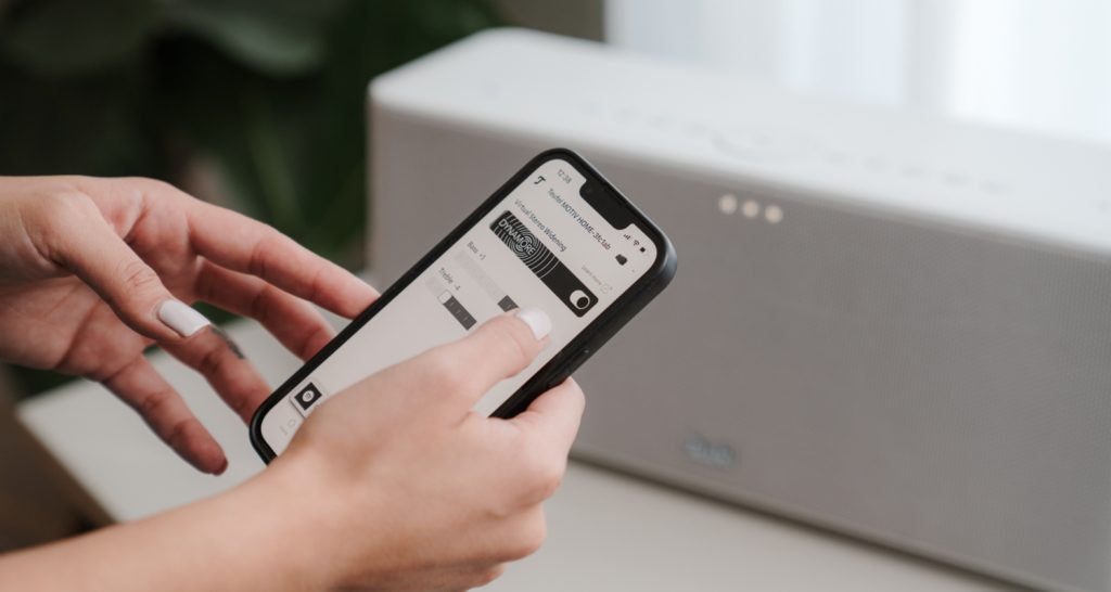 Une femme met la musique sur son enceinte MOTIV HOME avec son téléphone connecté.