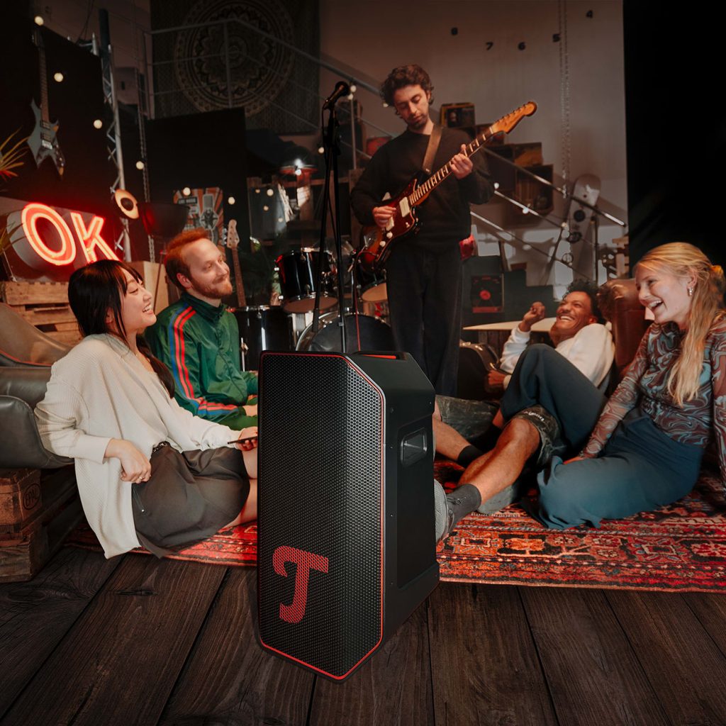 Un groupe de personnes et un guitariste dans une salle de répétition, avec le ROCKSTER AIR 2 de Teufel en avant-plan.